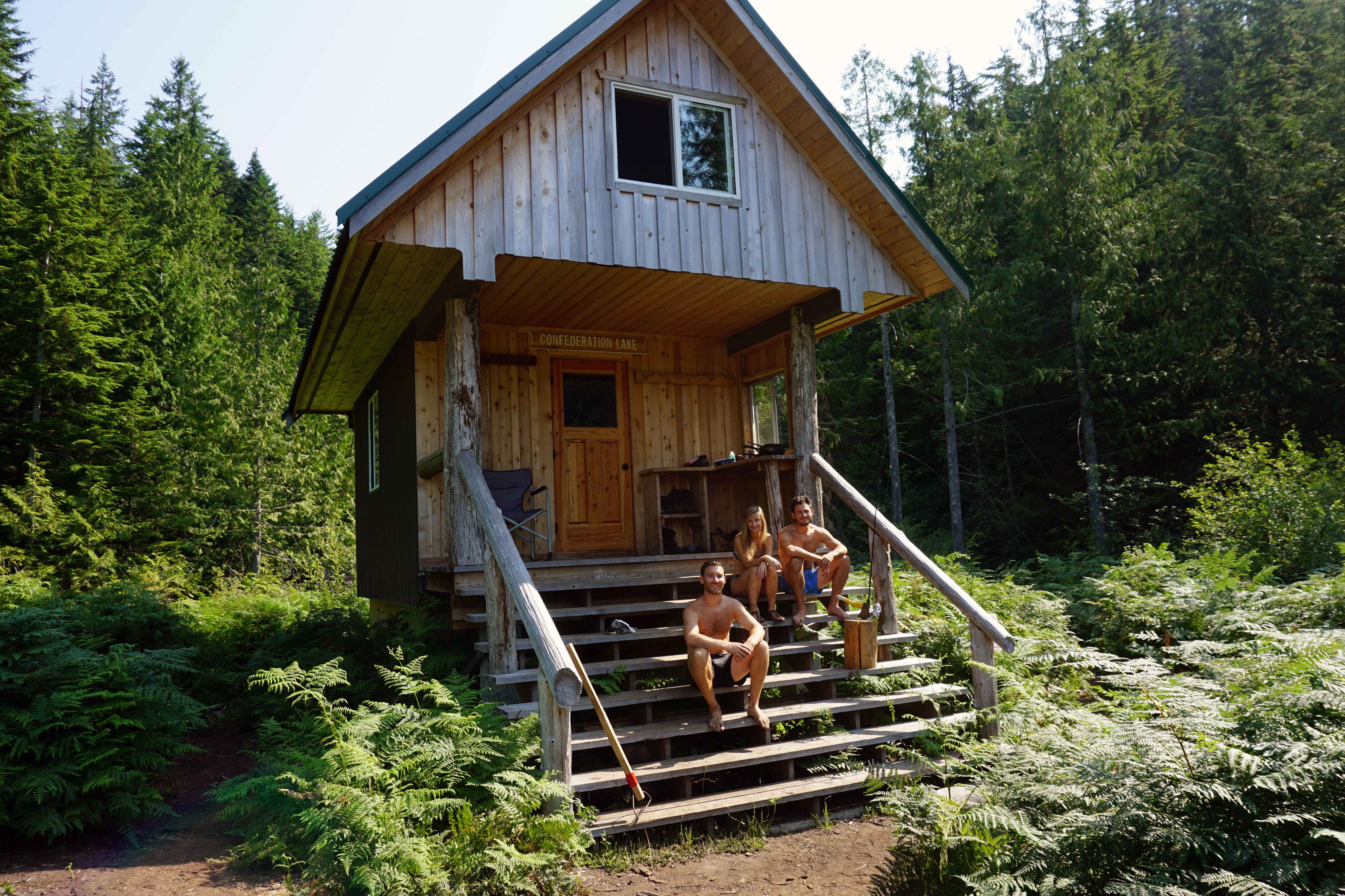 Three friends sit outside a wood cabin