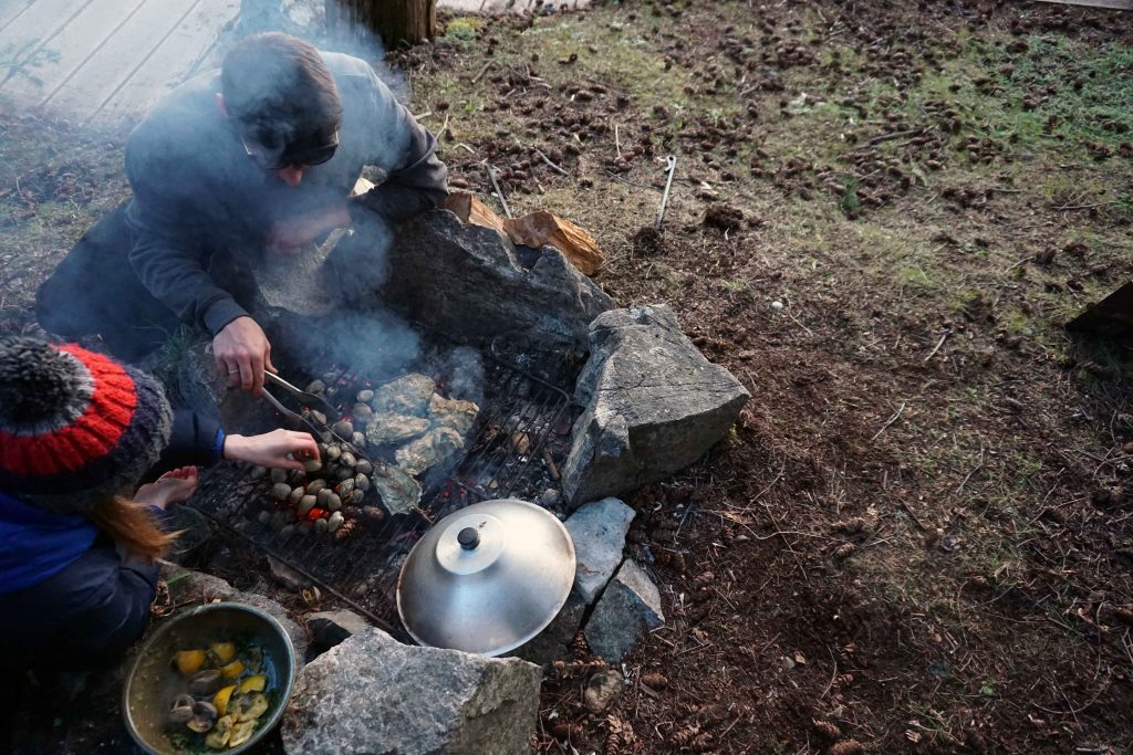 Man and woman cook oysters and clam on an outdoor fire