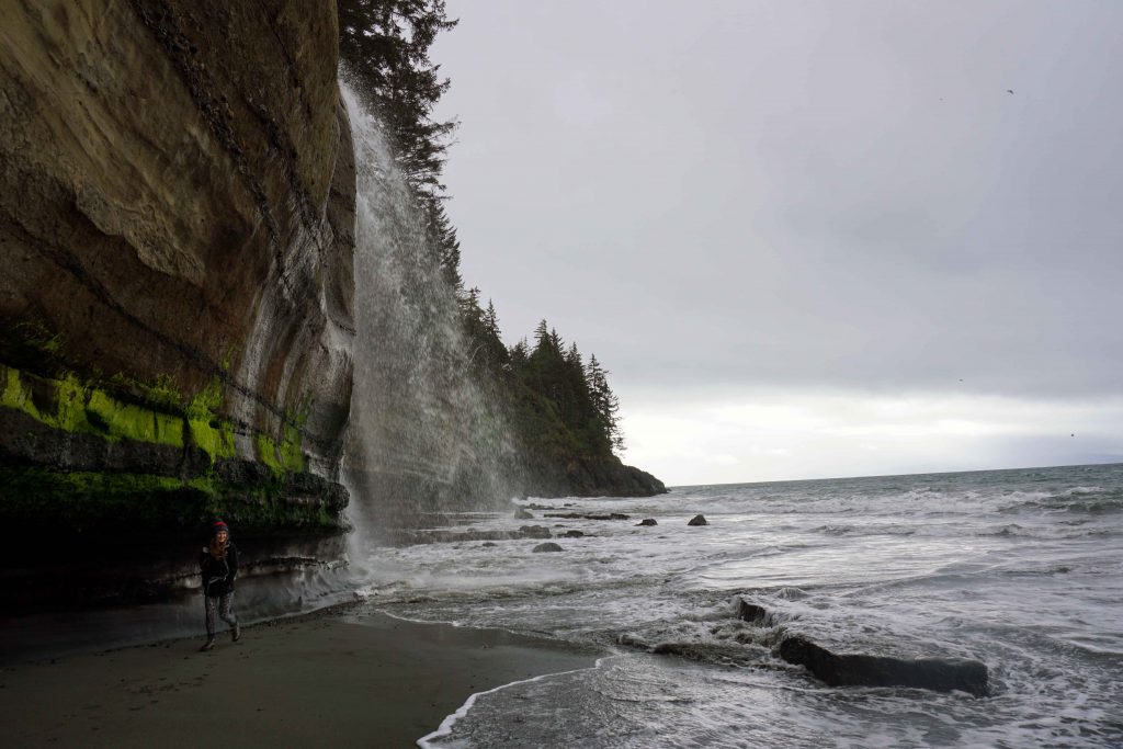 Woman stands by cliff next to waterfall