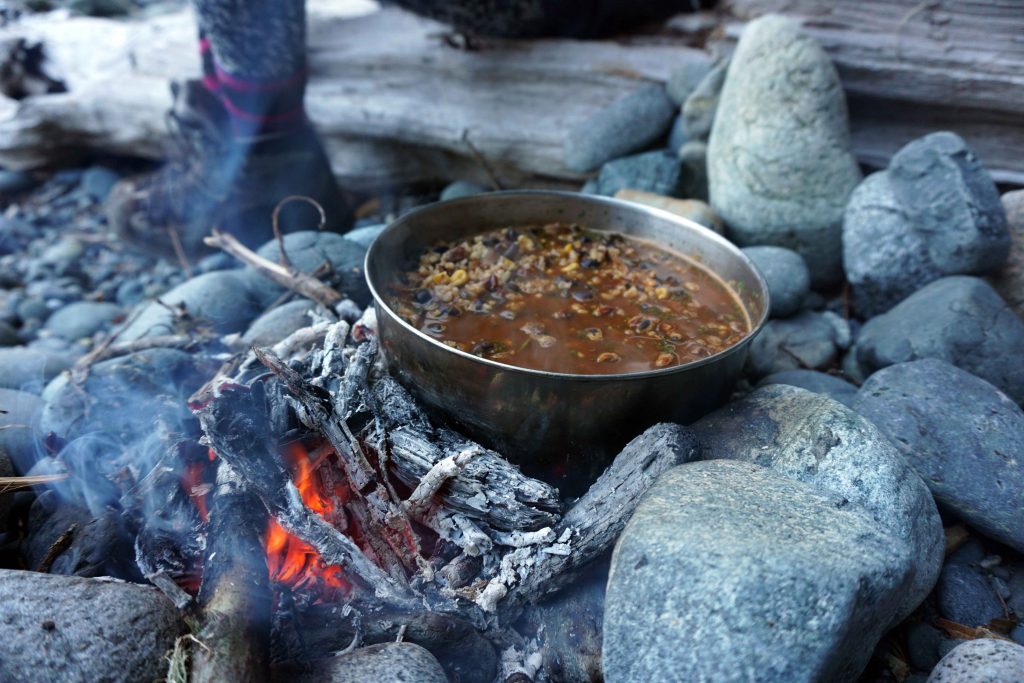 A saucepan full of stew heat on an open fire on a stony beach
