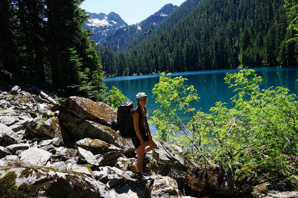 Woman stands on rock in front of blue lake