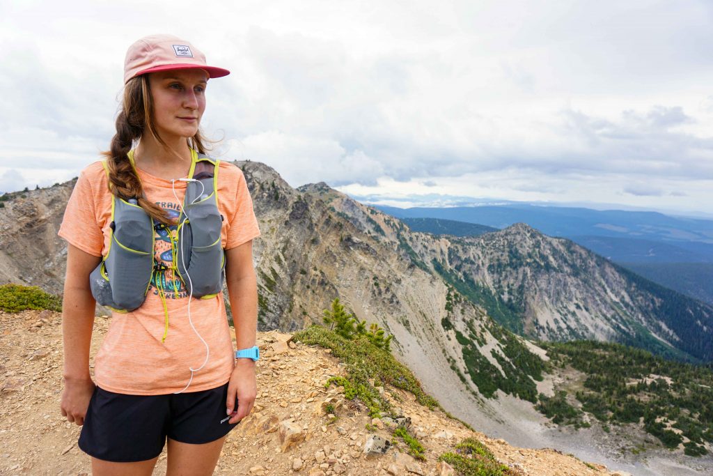 Woman stands on mountain wearing trail running vest