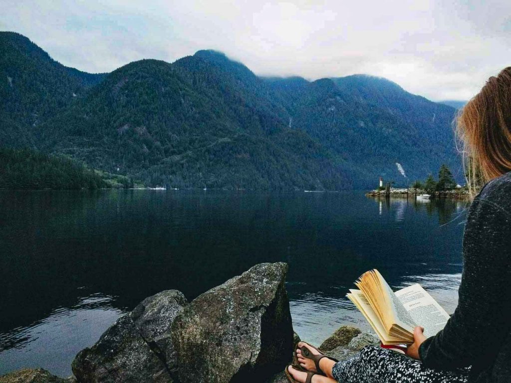 Woman reads book next to calm sea