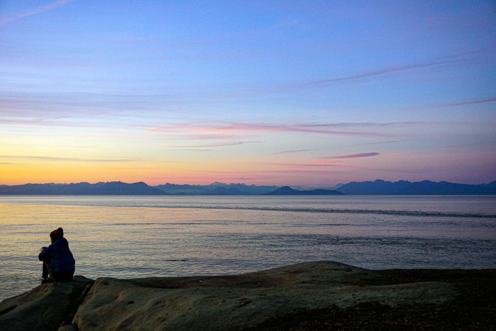 woman sits on rock at sunset