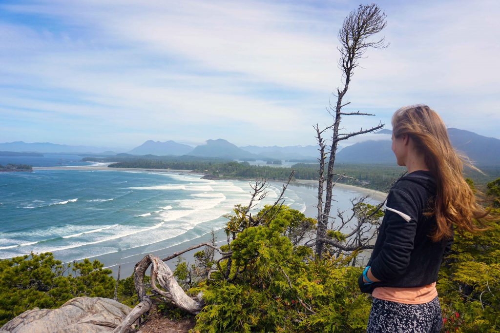 Woman on top of hill looks across sandy beach and sea with waves rolling in