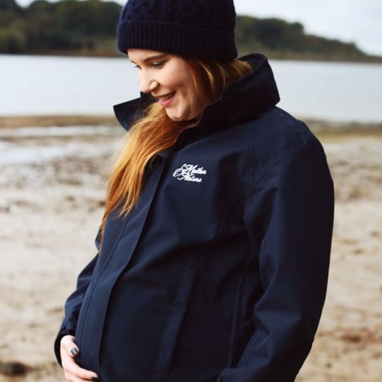 Pregnant woman holds bump while standing on beach