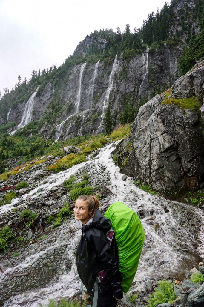 Woman wearing Osprey Sirrus backpack standing in front of waterfalls running off cliffs