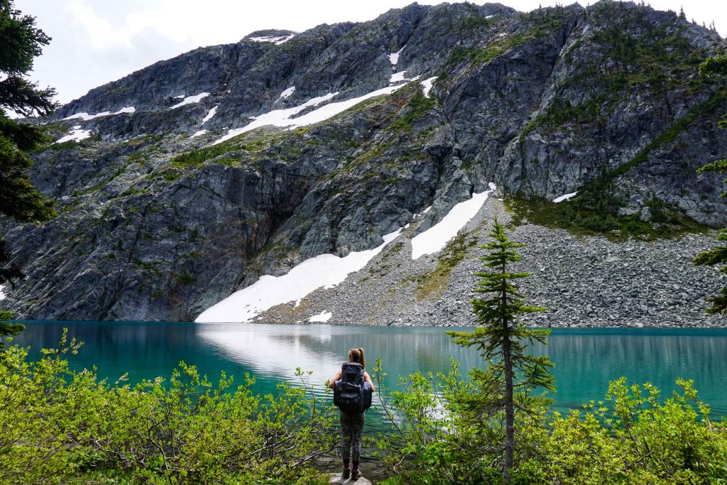 Woman wearing backpack stands in front of turquoise lake