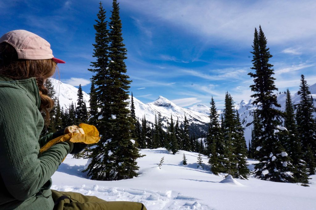 Woman in snowy mountain setting eats sandwich