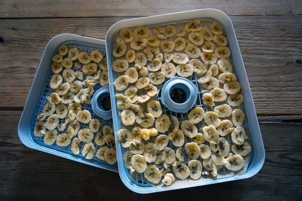 Chopped up banana in two dehydrator trays stacked on a wooden table