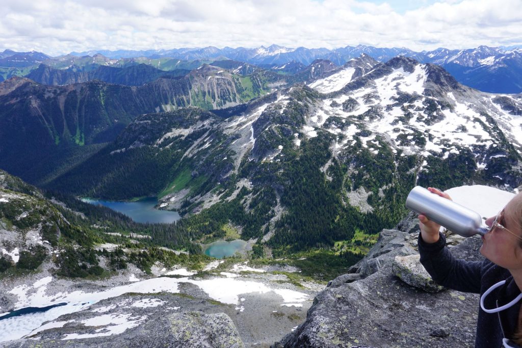 Woman sips from stainless steel bottle while on mountain summit