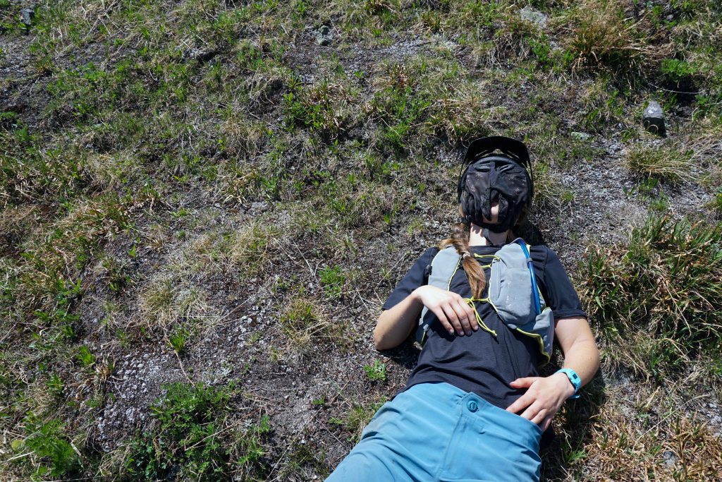 Woman lies on back on grass with gloves covering her face