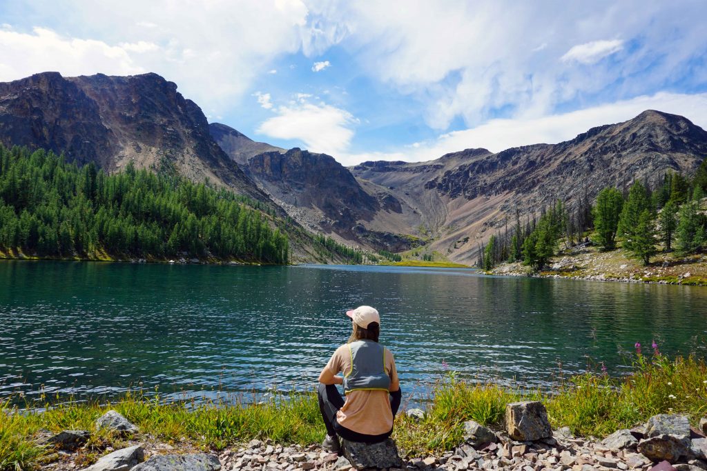Woman in running clothes sits next to alpine lake