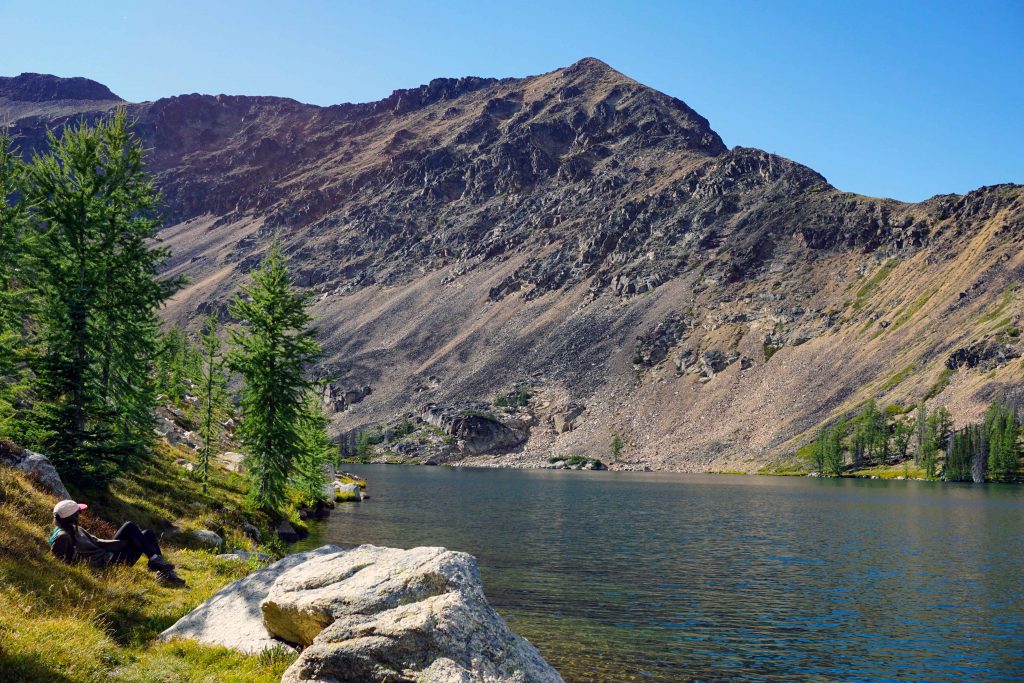 Woman relaxes in sunshine next to alpine lake