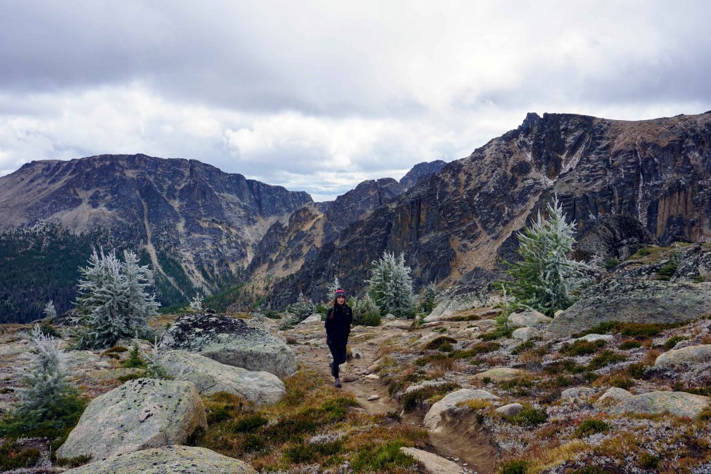 Woman hikes along stony trail with mountain vista behind her