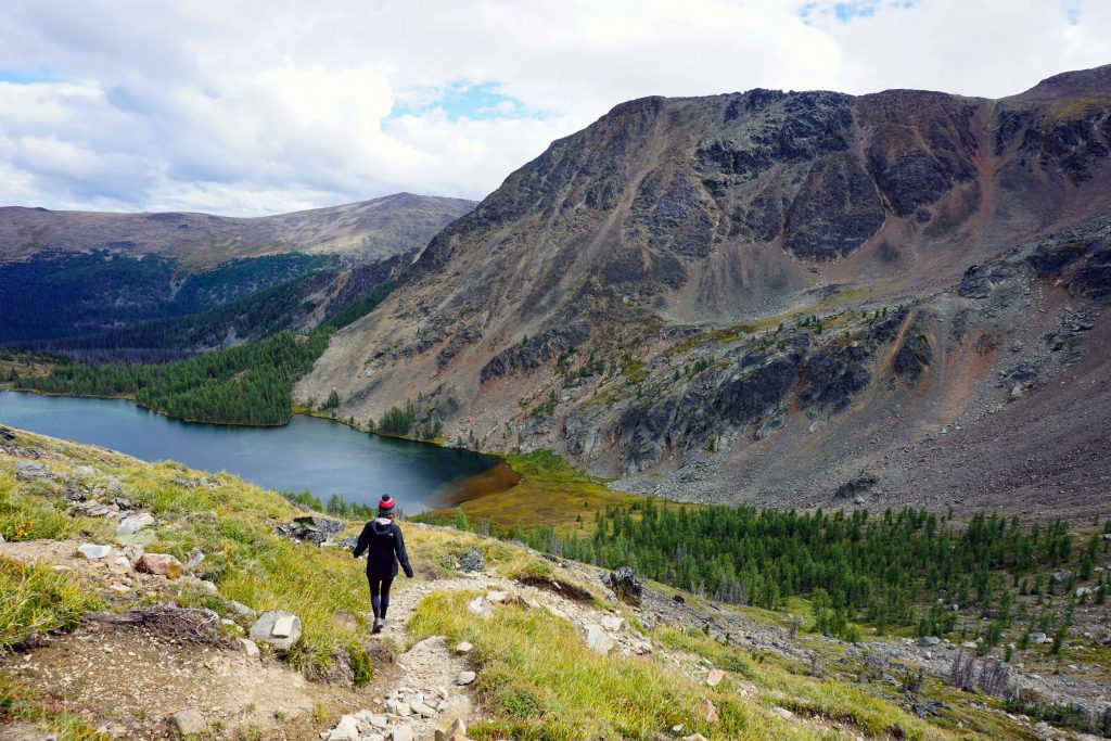 Woman hikes downhill towards alpine lake