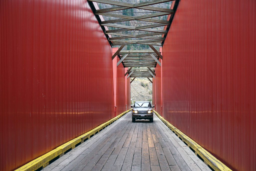 Silver car drives over red steel bridge