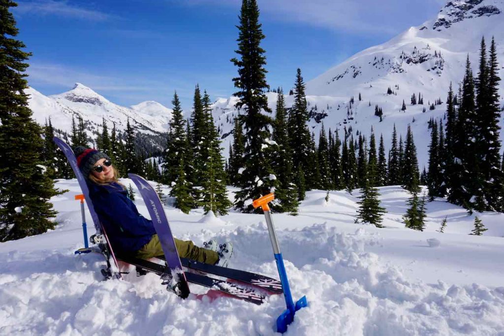 Woman sits on bench made out of skis surrounded by snowy mountains