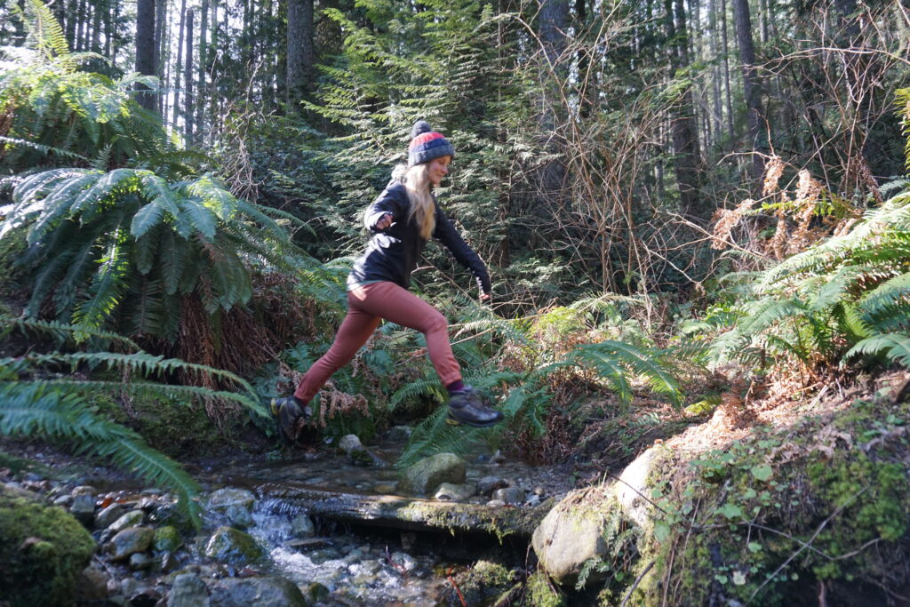 Woman jumps across a creek.